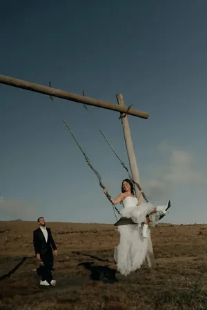 Wedding photo: bride on swing groom laughing field